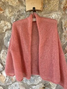 a pink sweater hanging on a stone wall with a wooden hanger in front of it