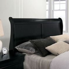 a bed with black headboard and pillows in a white room next to a window