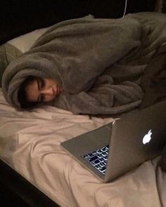 a man is sleeping in bed with his head on the pillow next to an apple laptop