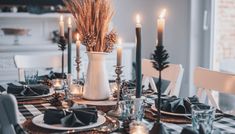 a dining room table set with black and white place settings, candles and napkins