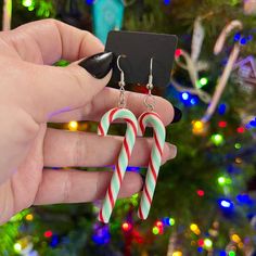 a hand holding two candy canes in front of a christmas tree