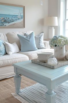 a living room filled with white furniture and blue pillows on top of a coffee table