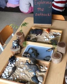 children are playing with dinosaurs in their sand and gravel trays at the table that is set up for an outdoor learning activity