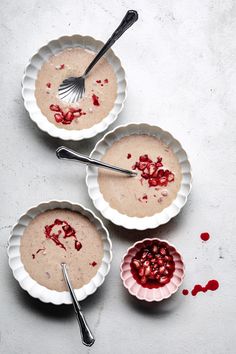 three bowls filled with pudding and topped with raspberry toppings next to a spoon