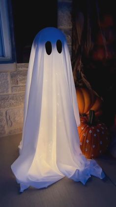 a white ghost sitting on top of a table next to pumpkins