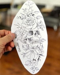 a person holding up a piece of paper with a skull and flowers on it