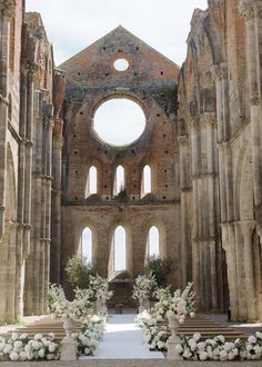 the inside of an old church with white flowers and greenery on the altars