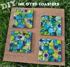 four square coasters sitting on top of a cork board covered in green and blue paint