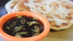 an orange bowl filled with food on top of a white plate next to a flat bread