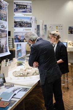 two people standing in front of a table with architectural models on it and posters behind them