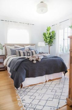 a bedroom with a bed, nightstands and plants in the window sill area