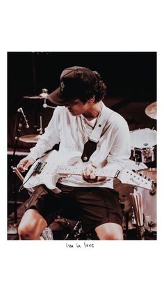 a man sitting in front of a drum set with his hands on an electric guitar