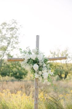 a cross decorated with white flowers and greenery for an outdoor wedding in the country