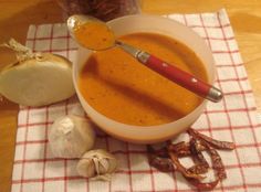 a bowl of soup with a spoon in it and garlic on the table next to it