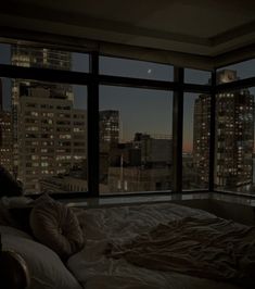 a person laying on a bed in front of a window with the city lights lit up