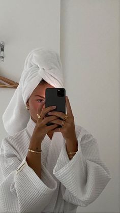 a woman taking a selfie in front of a mirror wearing a white towel on her head