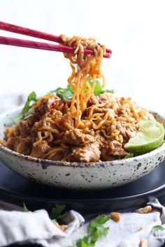 a bowl filled with noodles and meat on top of a black plate next to chopsticks