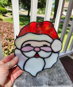 a hand holding up a stained glass santa clause ornament on a porch railing