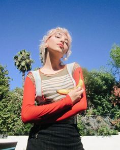 a woman standing with her arms crossed holding a banana and looking up at the sky