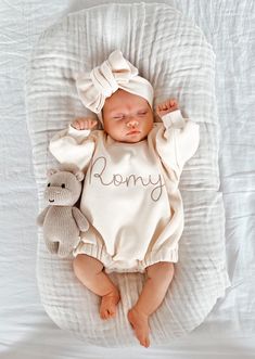 a baby is laying down with a teddy bear in it's arms and wearing a white romper