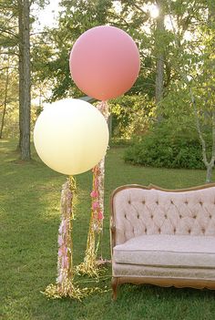 an old couch with balloons attached to it in front of a tree and lawn area