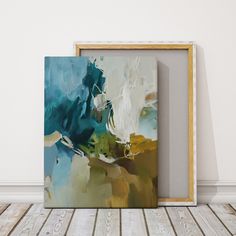 an abstract painting is displayed in front of a wooden frame on the floor, against a white wall