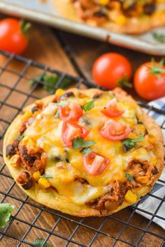 two pizzas sitting on top of a cooling rack next to some tomatoes and peppers