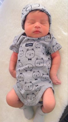 a baby laying on top of a white rug wearing a gray hat and bodysuit