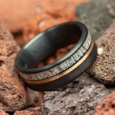 a wedding band with an antler wood and gold inlay is sitting on some rocks