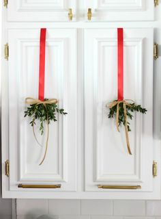 two white cabinets with christmas wreaths on the doors and red ribbon tied around them