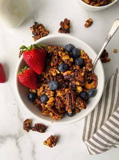 a bowl filled with granola and strawberries next to a glass of milk