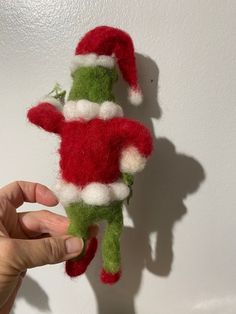 a hand is holding a small green and red stuffed animal with a santa hat on it's head