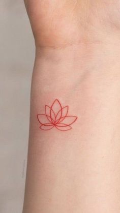 a red tattoo on the wrist of a woman with a lotus flower on her left arm