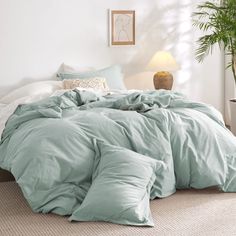 an unmade bed in a white bedroom with green comforter and pillows on the floor