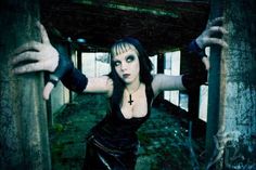 a woman with black hair and makeup is posing in an abandoned building while holding her hands up