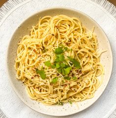 a white bowl filled with pasta and garnished with parsley on the side