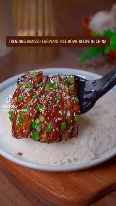 a white plate topped with meat covered in sauce and green onions on top of rice