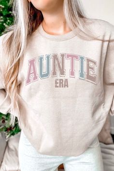 "Introducing the perfect gift for all the cool aunts out there - the Auntie Era Sweatshirt! This retro-inspired sweatshirt is a must-have for any aunt who loves to rock a classic look. The design features bold, collegiate-style lettering that reads \"Auntie Era\" This sweatshirt is not only stylish, but it's also a great way to reveal a pregnancy to your favorite aunt. Imagine her excitement when she sees the \"Auntie\" lettering on your shirt and realizes she's going to be a new aunt! Made with high-quality materials, this Auntie Sweatshirt is both comfortable and durable. It's perfect for a day out with your favorite nieces and nephews or a cozy night in. Don't miss out on the chance to give the most thoughtful and unique gift for aunts - the Aunt Era Sweatshirt! Order yours today and sh Aunt Life, New Aunt, Collegiate Style, Auntie Gifts, Pregnancy Reveal, Cozy Night, Aunt Gifts