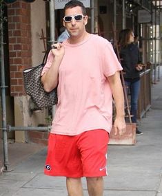 a man in pink shirt and red shorts walking down the street