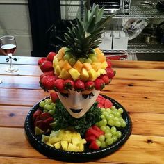 a plate with fruit on top of it and a mask made out of grapes, strawberries, pineapples