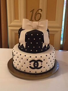 a black and white cake with polka dots and a chanel logo on top is sitting on a table in front of a doorway