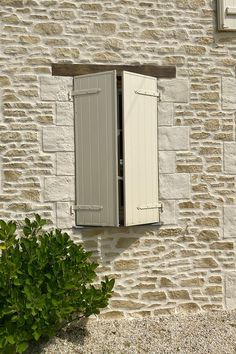 an open window on the side of a stone building with green plants in front of it