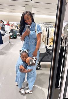 a woman in overalls taking a selfie with her daughter, who is holding a cell phone