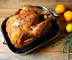 a roasted turkey in a cast iron pan with lemons and herbs next to it