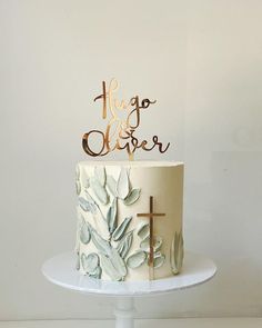 a cake with a cross on top is sitting on a white plate and has gold lettering that says hug us closer