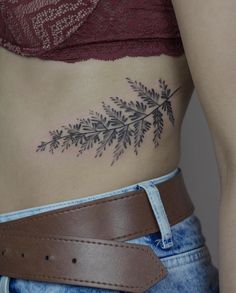 a woman's stomach with a tattoo on the side that has leaves and branches drawn on it