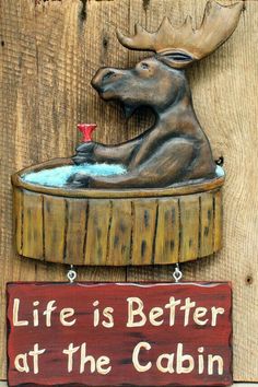 a sign that says life is better at the cabin with a moose sitting in a bathtub