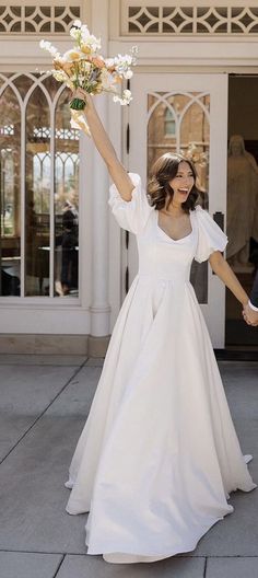 a bride and groom hold hands as they walk down the street holding flowers in their hand