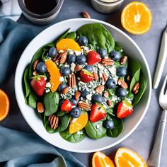 a white bowl filled with spinach, blueberries, oranges and pecans