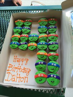 a box filled with green cupcakes covered in icing